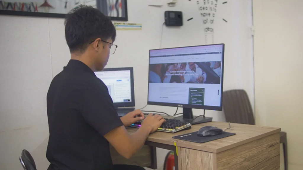 A team member working on a website or digital project using a desktop computer in a shared workspace.